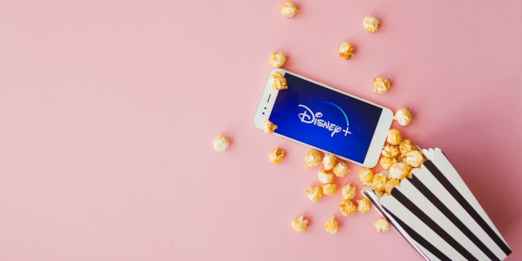 Disney Logo On Phone With Box Of Popcorn On Pink Background.jpg