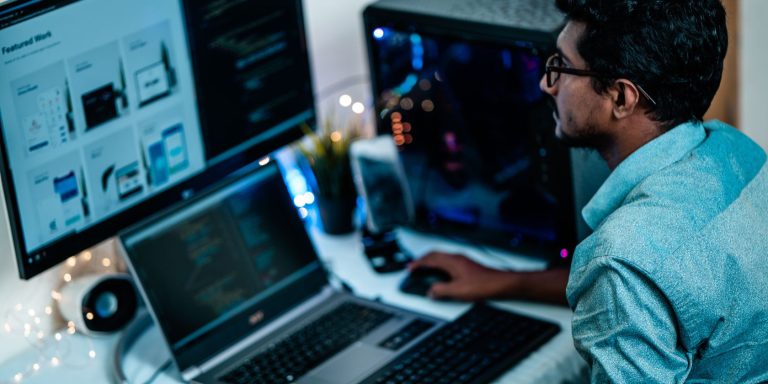 A Man Uses His Laptop And A Desktop Computer For Work.jpg